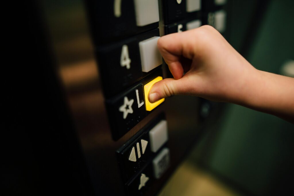 A close-up shot of a hand pushing the 'L' button in an elevator, indoors.